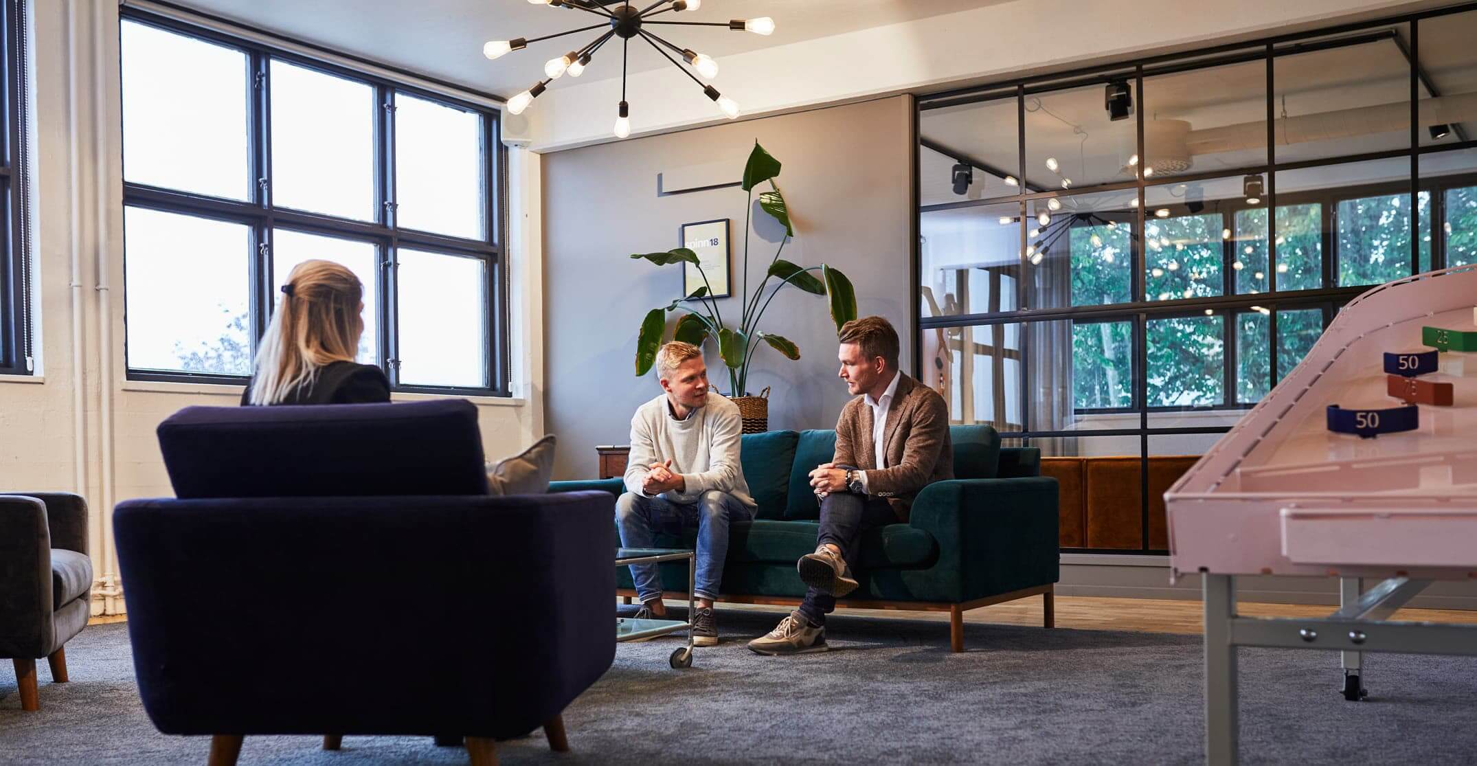 Tre personer i soffgrupp på kontor